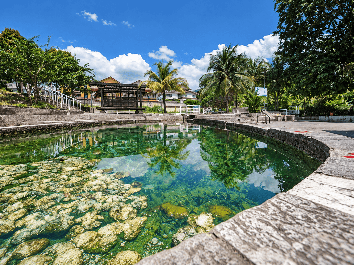 The natural hot spring pool at Selayang Hot Spring, Selangor, with clear turquoise water, palm trees and a covered pavilion