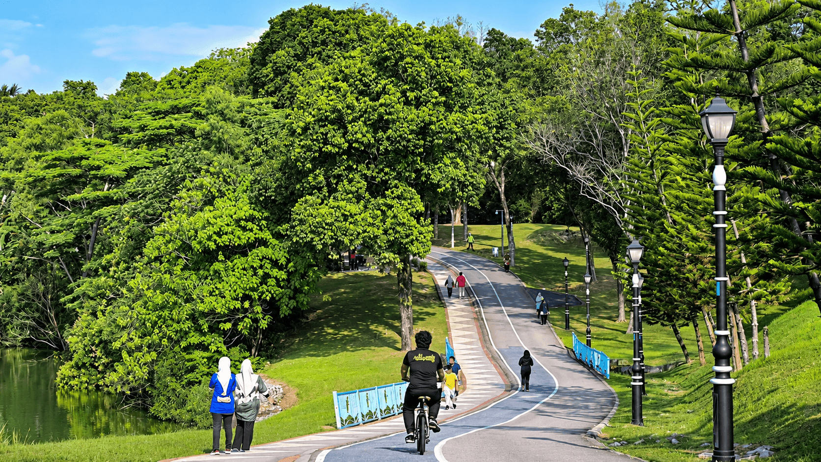 Cyclists and walkers on the lakeside path through Kepong Metropolitan Park, Kuala Lumpur, surrounded by mature trees