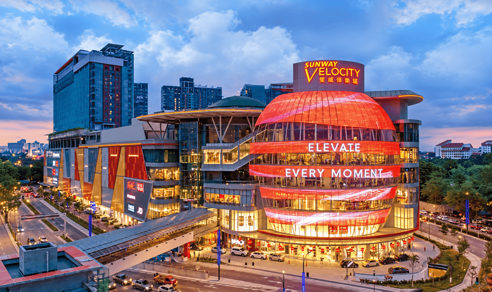 Sunway Velocity Mall lit up at dusk in Cheras, Kuala Lumpur, with its red spherical facade and surrounding high-rise towers